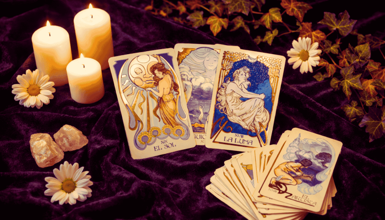 Mesa con mantel de terciopelo con decoraciones florales y tres velas blancas enmarcando un mazo de cartas de tarot blanco y dorado
